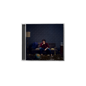 CD jewel case in plastica di michele bravi con foto di copertina del cantante seduto su un divano con sfondo di moquette blu e mappamondo in primo piano