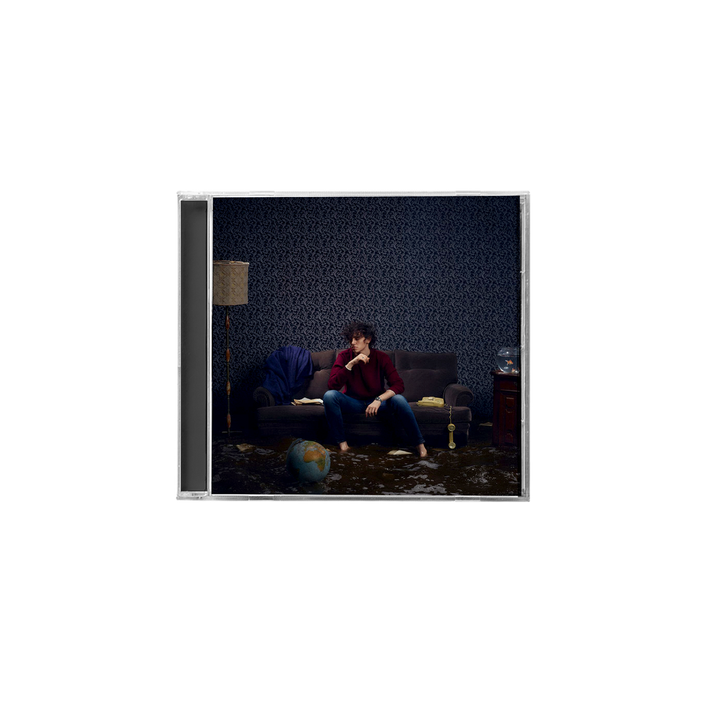 CD jewel case in plastica di michele bravi con foto di copertina del cantante seduto su un divano con sfondo di moquette blu e mappamondo in primo piano