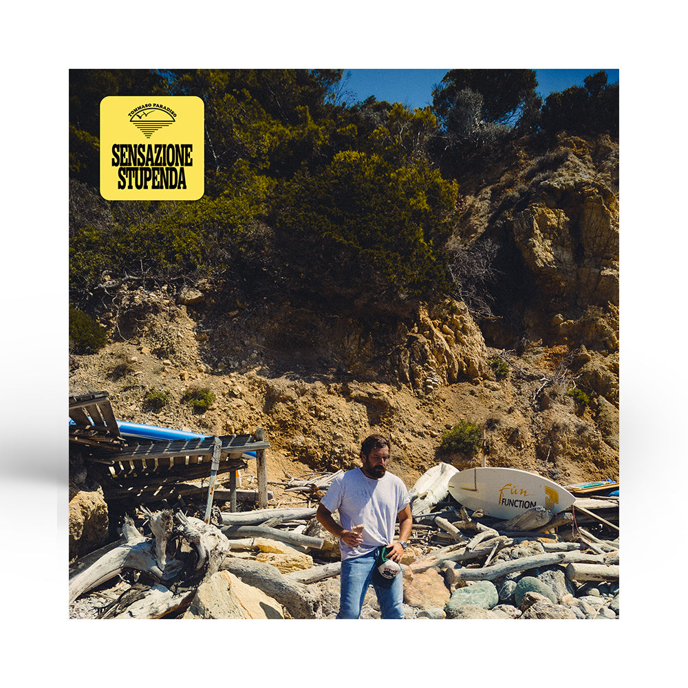 immagine di copertina di tomasso paradiso nuovo album sensazione stupenda si vede un uomo di mezza età in una spiaggia dove si intravedono dei grossi legni e una tavola da surf